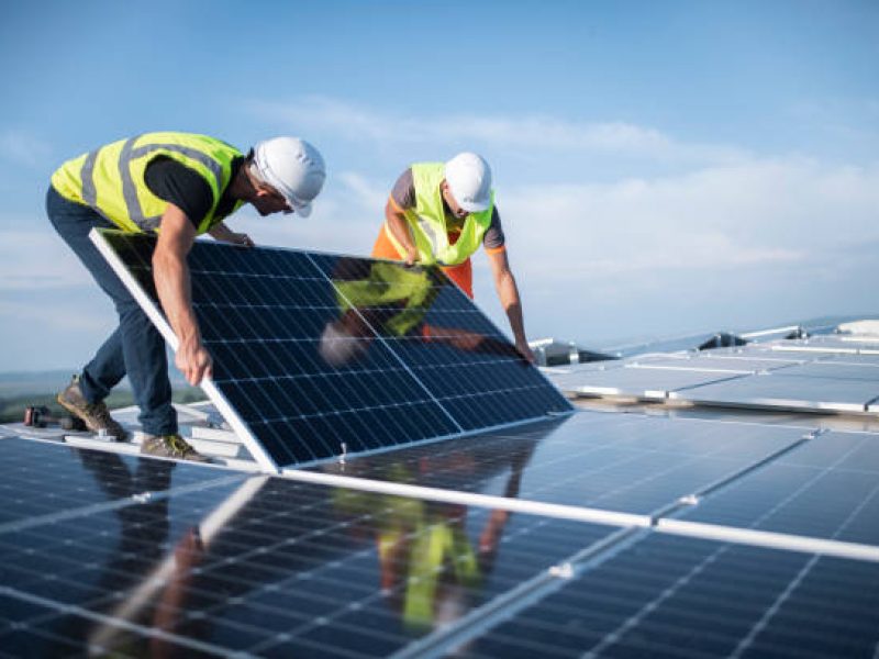 Team of two engineers installing solar panels on roof.